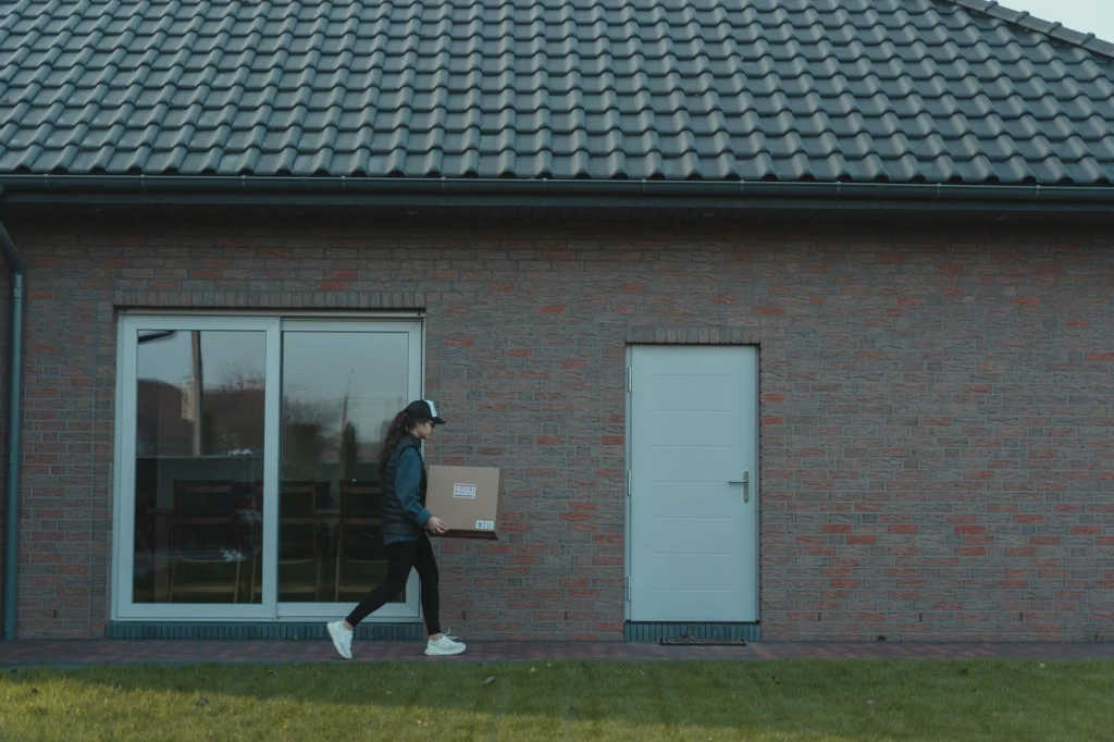 Verhuizer draagt een doos naar een bakstenen huis