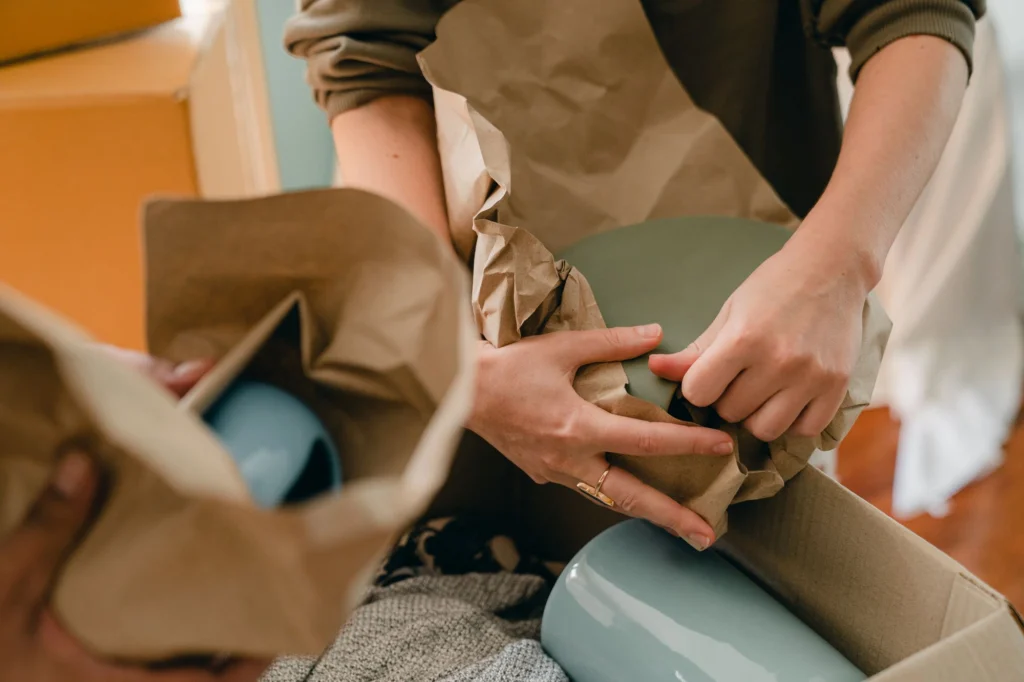 Handen pakken breekbare spullen in papier